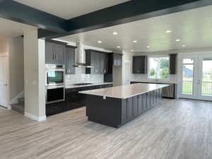 Kitchen with a center island, stainless steel appliances, light stone counters, light wood-style floors, and tasteful backsplash