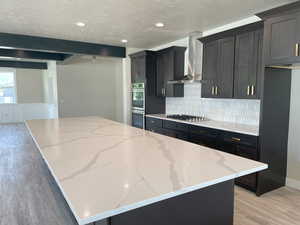 Kitchen featuring a kitchen island, light wood-style flooring, dark cabinets, light stone counters, and recessed lighting