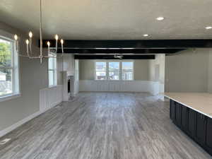 Unfurnished living room featuring a textured ceiling, light wood-style flooring, a fireplace, a wainscoted wall, and suspended lighting