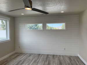 Spare room featuring light wood-type flooring, wood walls, a textured ceiling, ceiling fan, and recessed lighting
