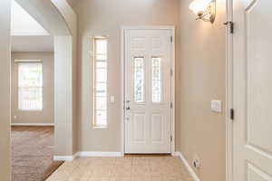 Foyer entrance featuring arched walkways, light tile patterned floors, and light carpet