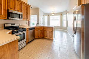 Kitchen featuring stainless steel appliances, light countertops, wood finish cabinetry, a peninsula, and light tile patterned floors