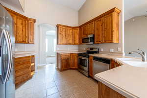 Kitchen with stainless steel appliances, arched walkways, wood finish cabinets, light countertops, and vaulted ceiling