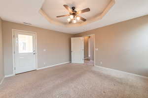 Unfurnished bedroom featuring carpet, ceiling fan, and a tray ceiling