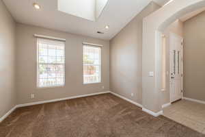 Carpeted empty room featuring arched walkways, recessed lighting, a skylight, vaulted ceiling, and tile patterned flooring