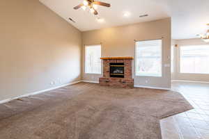 Unfurnished living room featuring light tile patterned floors, light colored carpet, ceiling fan, a fireplace, and lofted ceiling
