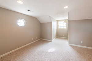 Bonus room with vaulted ceiling and light carpet