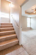 Stairs featuring ceiling fan, carpet floors, and a tray ceiling