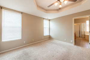 Unfurnished room with ceiling fan, light colored carpet, and a tray ceiling