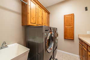 Laundry room with cabinet space, washer and dryer, light tile patterned floors, and a textured wall