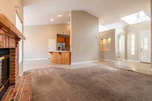 Unfurnished living room featuring light carpet, lofted ceiling, light tile patterned floors, a fireplace, and arched walkways