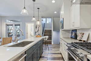 Kitchen featuring dual tone cabinetry, stainless steel appliances, decorative light fixtures, light stone counters, and light wood-style floors