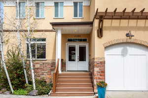 Entrance to property with french doors, covered porch, stucco siding, and stone siding