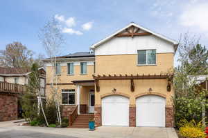 View of front of home with roof mounted solar panels, an attached garage, concrete driveway, board and batten siding, and stucco siding