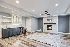 Indoor wet bar featuring glass insert cabinets, two tone color scheme, open shelves, wine cooler, and a fireplace