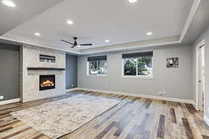 Unfurnished living room with a tray ceiling, a tile fireplace, light wood finished floors, ceiling fan, and recessed lighting
