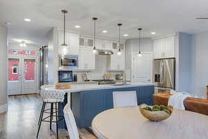 Two tone kitchen with stainless steel appliances, glass fronted cabinets, two tone cabinets, an island with sink, and light wood-style flooring