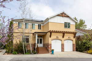 View of front of property with roof mounted solar panels, stone siding, a garage, concrete driveway, and board and batten siding