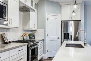 Kitchen featuring stainless steel appliances, white cabinetry, and decorative light fixtures