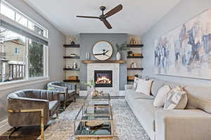 Living room with ceiling fan, a stone fireplace, and wood finished floors