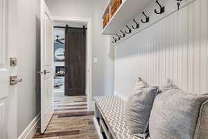 Mudroom featuring a barn door, a stone fireplace, wood finished floors, and a ceiling fan