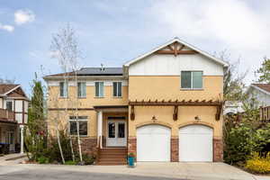 View of front of house with roof mounted solar panels, a garage, stone siding, driveway, and stucco siding