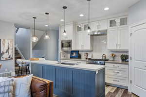 Two tone kitchen with dark wood finished floors, backsplash, pendant lighting, dual tone cabinetry, and a center island with sink