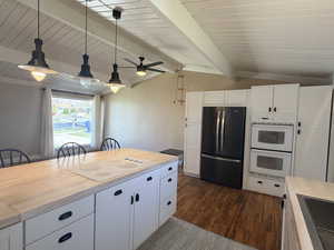 Kitchen featuring white appliances, white cabinetry, vaulted ceiling with beams, decorative light fixtures, and dark wood-type flooring
