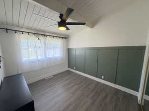 Empty room with a decorative wall, wooden ceiling, vaulted ceiling with beams, a wainscoted wall, and ceiling fan