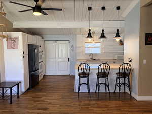 Kitchen with a kitchen bar, light countertops, white appliances, hanging light fixtures, and a peninsula