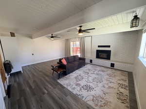 Living area with dark wood-type flooring, a brick fireplace, brick wall, a ceiling fan, and heating unit