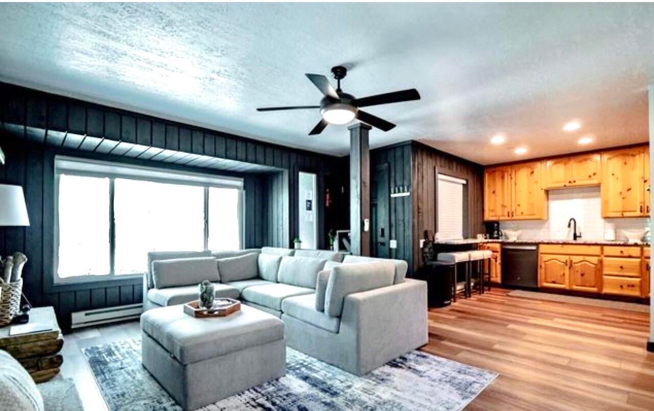 Living room with ceiling fan, light wood finished floors, baseboard heating, and wooden walls