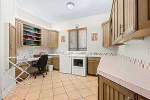 Laundry area with an office area, washing machine and dryer, light tile patterned floors, and cabinet space