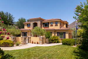 Mediterranean / spanish home featuring stone siding, a gate, a fenced front yard, stucco siding, and a tile roof