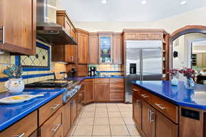 Kitchen featuring wood finish cabinetry, stainless steel appliances, light tile patterned flooring, decorative backsplash, and recessed lighting
