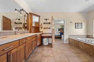 Ensuite bathroom featuring double vanity, a bath, and light tile patterned floors