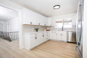 Kitchen with stainless steel appliances, white cabinets, backsplash, light wood-style flooring, and light stone countertops