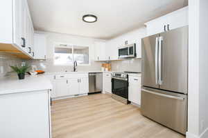 Kitchen with stainless steel appliances, white cabinets, light wood finished floors, and light stone counters