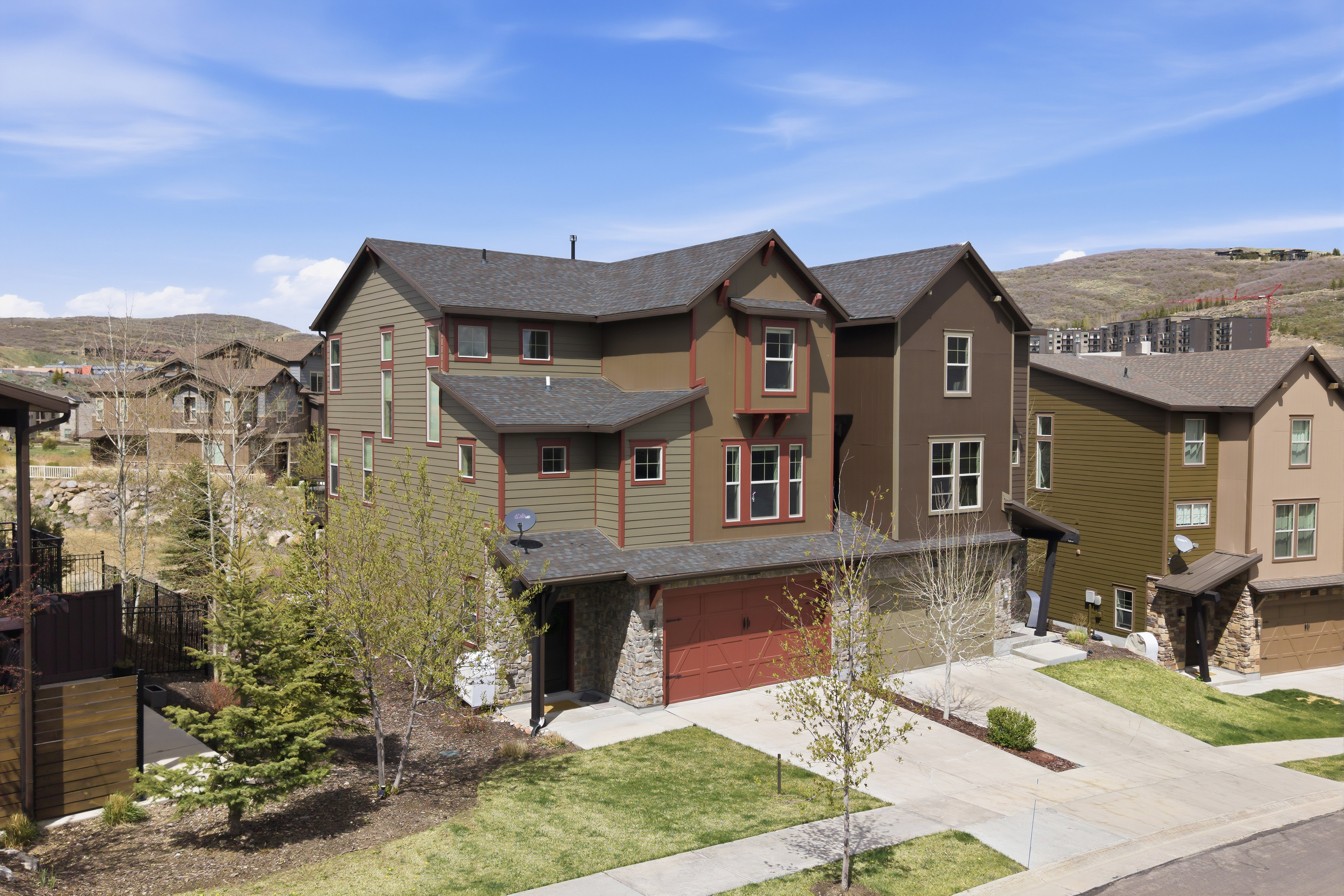 Multi-story residence featuring composite siding, stone veneer accents, and a red garage door
