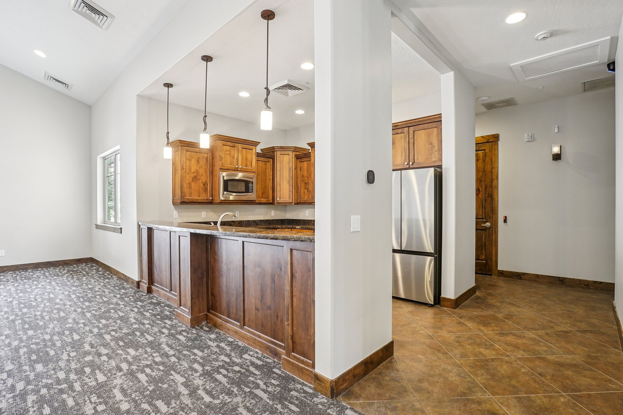 Kitchen with pendant lighting, stainless steel appliances, dark stone countertops, and wood finish cabinetry