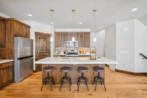 Kitchen featuring an island with sink, pendant lighting, a breakfast bar, stainless steel appliances, and light wood-style flooring