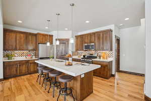 Kitchen featuring hanging light fixtures, light wood-type flooring, stainless steel appliances, and a breakfast bar area