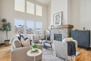 Living room featuring light wood-style flooring, a stone fireplace, and a high ceiling