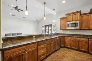 Kitchen with lofted ceiling, wood finish cabinetry, decorative light fixtures, stainless steel appliances, and a peninsula
