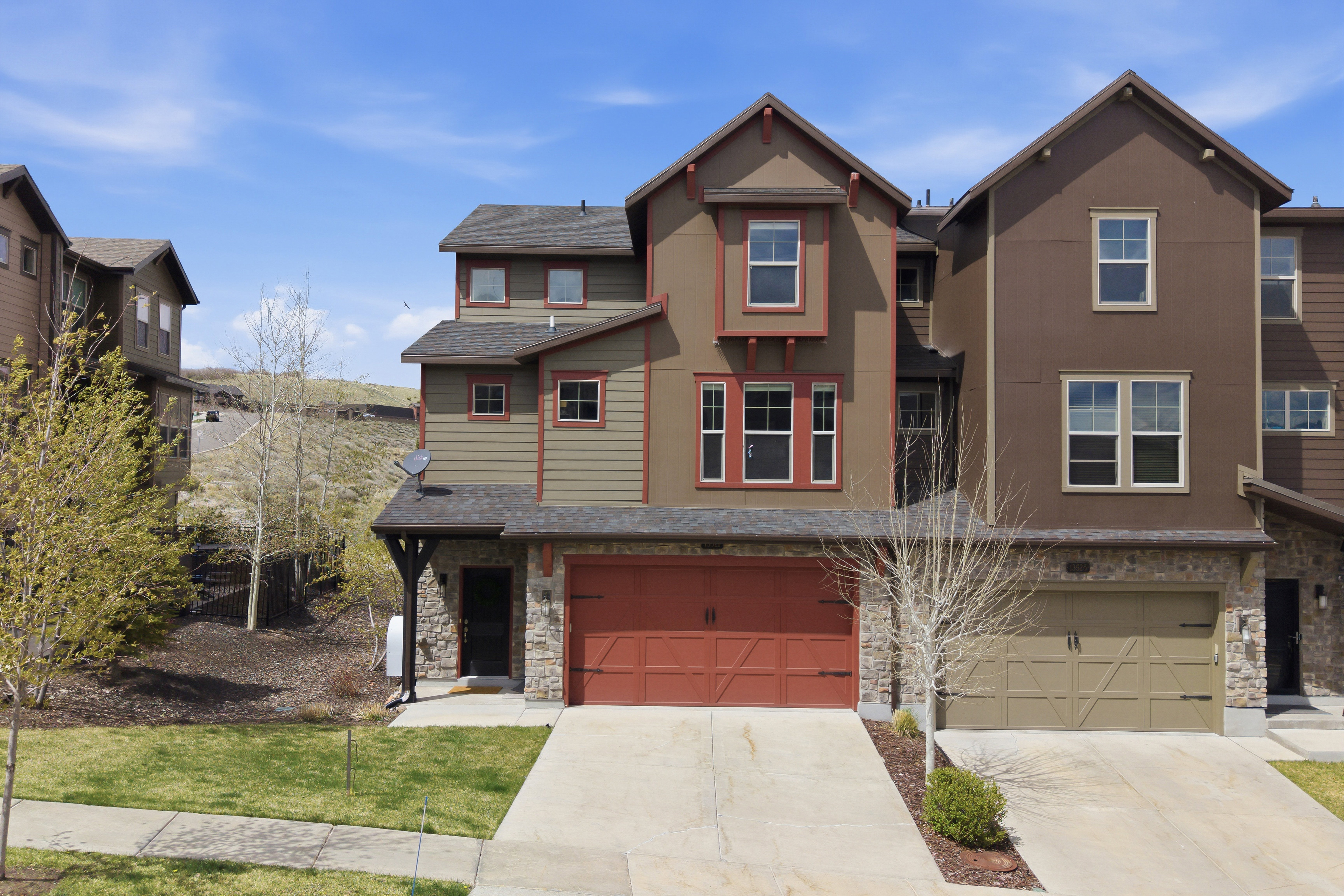 Multilevel townhome featuring a stone facade, red garage door, and contrasting trim accents