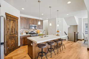 Kitchen with pendant lighting, a kitchen bar, stainless steel appliances, light wood-style floors, and a kitchen island with sink