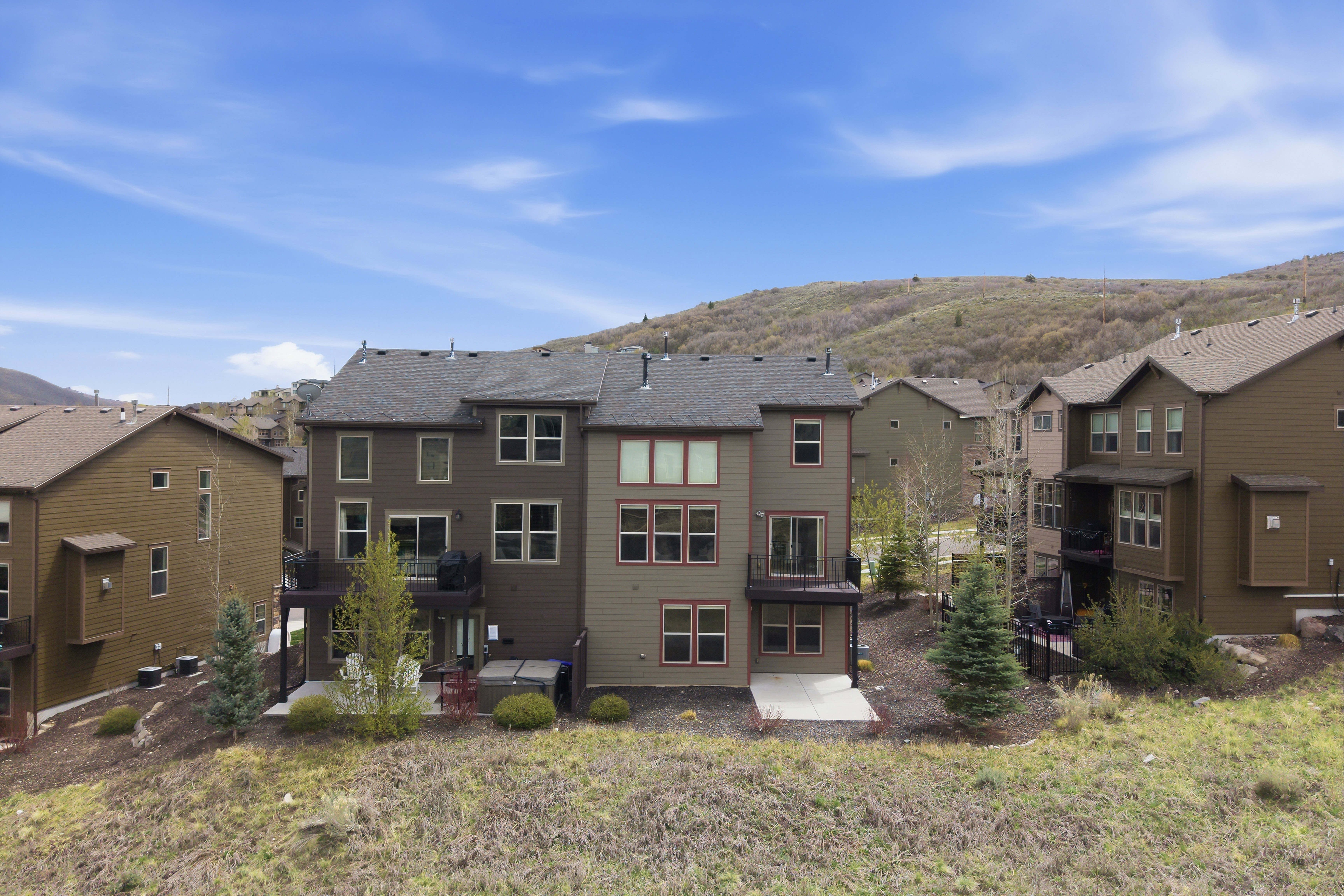 Rear exterior featuring multi-level decks, a ground-level concrete patio, and a sloped landscape with mature trees