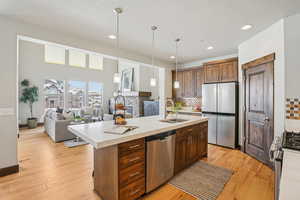 Kitchen featuring decorative light fixtures, open floor plan, stainless steel appliances, decorative backsplash, and light wood-style flooring