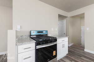 Kitchen with white cabinetry, stainless steel range with gas stovetop, light stone countertops, a textured ceiling, and dark wood-style flooring