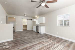 Kitchen featuring a barn door, white cabinetry, dark wood-style flooring, stainless steel dishwasher, and a textured ceiling
